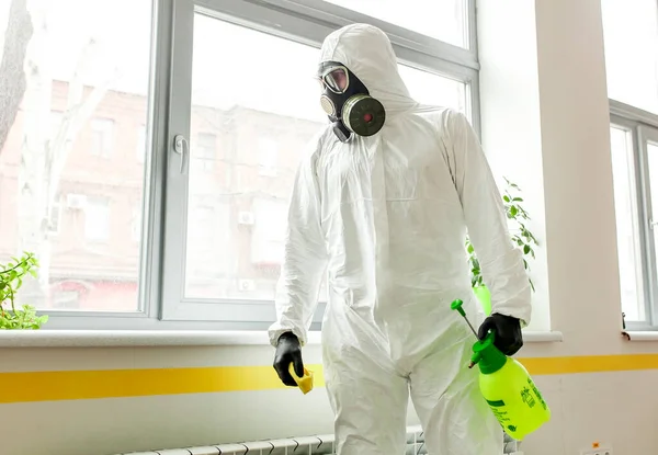 保護具の男がオフィスでスプレーで消毒します コロナウイルスCovid 19疾患による表面処理 白いスーツの男がスプレー銃で部屋を消毒します ウイルスのパンデミック — ストック写真