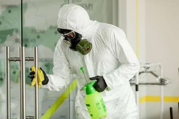 Koruyucu ekipmanlı bir adam ofiste spreyle dezenfekte ediyor. Coronavirus covid-19 hastalığından dolayı yüzey tedavisi. Beyaz takım elbiseli bir adam odayı sprey silahla dezenfekte ediyor. Virüs salgını