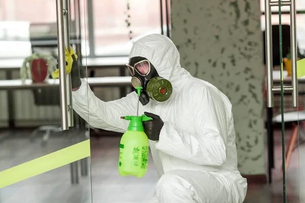 A man in protective equipment disinfects with a sprayer in the office. Surface treatment due to coronavirus covid-19 disease. A man in a white suit disinfects the room with a spray gun. Virus pandemic