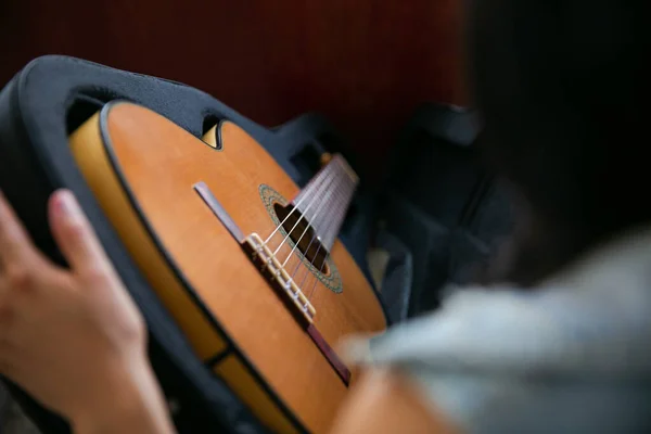 Kadın siyah bir çantadaki klasik kahverengi gitarı gözlemler ve çıkarır.