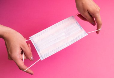 Ellerindeki pembe arka planda tıbbi, cerrahi maske.