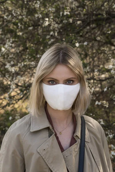 SARS-CoV-2 virüsü yaydığı için koruyucu maskeli genç sarışın kız. Salgın hastalık. Coronavirus. Covid-19. Arka planda ağaçlar.