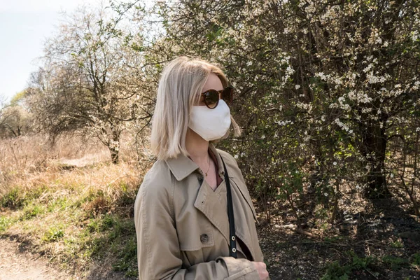 SARS-CoV-2 virüsü yaydığı için koruyucu maskeli genç sarışın kız. Salgın hastalık. Coronavirus. Covid-19. Arka planda ağaçlar.