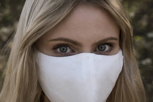 SARS-CoV-2 virüsü yaydığı için koruyucu maskeli genç sarışın kız. Salgın hastalık. Coronavirus. Covid-19. Arka planda ağaçlar.