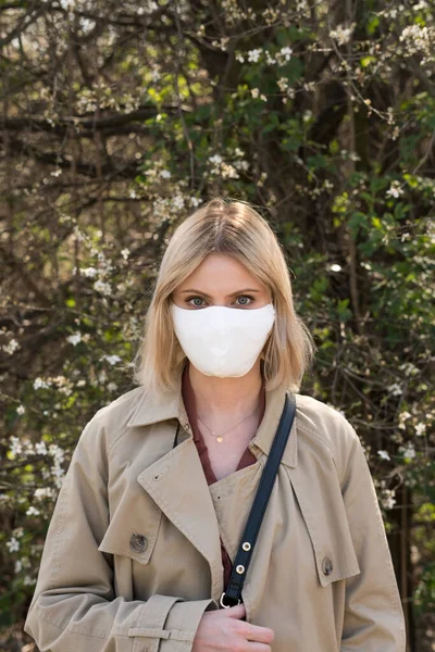 SARS-CoV-2 virüsü yaydığı için koruyucu maskeli genç sarışın kız. Salgın hastalık. Coronavirus. Covid-19. Arka planda ağaçlar.