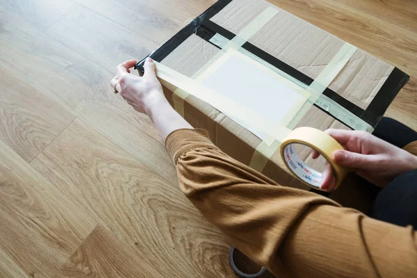 Müşteri olan genç bir kadın paket hazırlıyor. Bant ve makas kullanarak. Kız tüketici yerde karton kutu tutuyor..