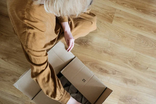 Müşteri olan genç bir kadın paket hazırlıyor. Bant ve makas kullanarak. Kız tüketici yerde karton kutu tutuyor..