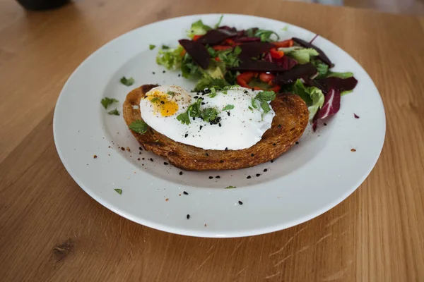 Bir parça ekmeğin üzerinde haşlanmış yumurta, tabakta yeşil salata ve ahşap masanın üzerinde. Sağlıklı Kahvaltı