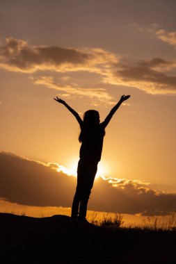 Gün batımında tarlada elleri havada kızların siluetleri.