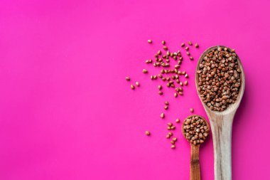 Ahşap kaşık dolusu kavrulmuş karabuğday karabuğday, karabuğday kavanozu arka planında, sağlıklı beslenme için glütensiz kadim tahıl, seçici odaklanma. Coronavirus gıda malzemeleri. Pembe bir arka planda. en üstteki görünüm.