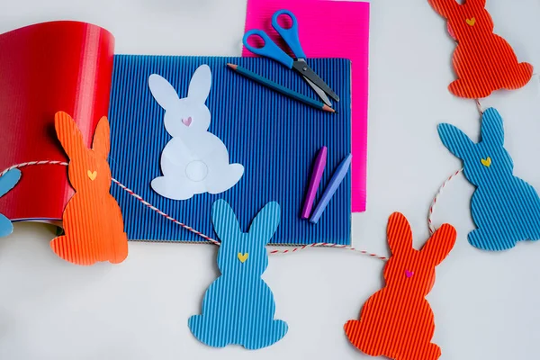 DIY праздничная гирлянда из разноцветных лебедок и ремесленных инструментов. Шаблон кролика на Пасху сделать это самостоятельно. Руки детей. Творческий процесс. Пасхальная бумага для украшения кроликов . — стоковое фото