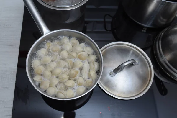 Ravioli in der Pfanne, kochendes Wasser, silberner Metallhintergrund. Pelmeni, mit Hackfleisch gefüllte russische Knödel, im Stahltopf auf Keramikherd in der heimischen Küche. Varenyky, Vareniki. — Stockfoto