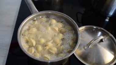 Tavada Ravioli, kaynar su, gümüş metal arka plan. Pelmeni pişirmek, kıyma ile doldurulmuş Rus köfteleri, ev mutfağındaki seramik ocağın çelik güvecinde. Varenyky, vareniki.