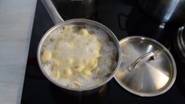 Tavada Ravioli, kaynar su, gümüş metal arka plan. Pelmeni pişirmek, kıyma ile doldurulmuş Rus köfteleri, ev mutfağındaki seramik ocağın çelik güvecinde. Varenyky, vareniki.