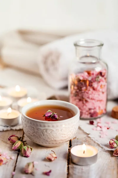 Concept of spa treatment with roses. Herbal tea, crystals of sea pink salt in bottle, candle as decor. Atmosphere of relax, anti-stress and detox procedure. Luxury lifestyle. Wooden background