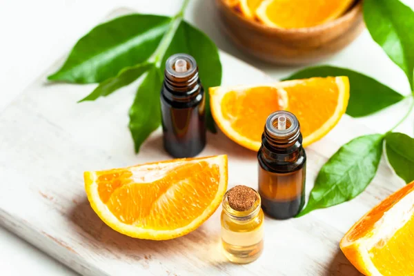 Concept of natural organic orange essential oil for skin face and body health care. Moisturizing, aromatherapy, detox treatment, anti-stress effect. Fresh fruit, green leaves, white background