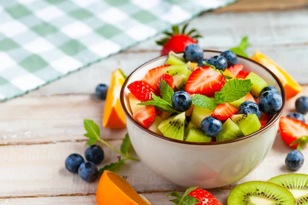 Concept of low calories delicious desserts. Summer fresh bowl with colorful fruit salad. Healthy natural organic food. Tasty sweet snack, light simple tasty lunch. Close up macro view wooden backgroun