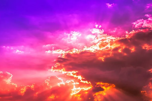 Bright Sun light behind red clouds in purple blue sky with pink and orange light