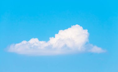 Masmavi gökyüzünde güneş ışığıyla süzülen yalnız, tüylü bulutlar.