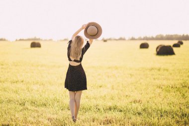 Gün batımında elinde şapkasıyla tarlada bir kız.