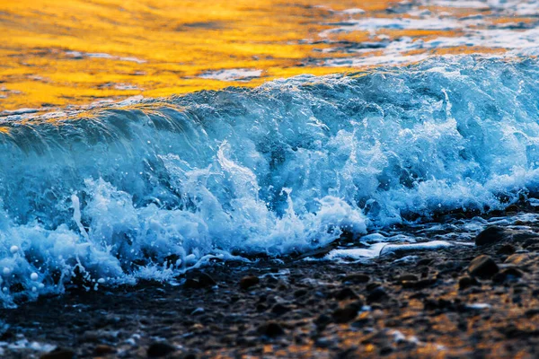 Köpüklü güzel dalgalar, denizin batan güneşiyle aydınlanıyor. Gün batımında dalgalı deniz yüzeyinin dokusu.