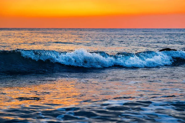 Köpüklü güzel dalgalar, denizin batan güneşiyle aydınlanıyor. Gün batımında dalgalı deniz yüzeyinin dokusu.