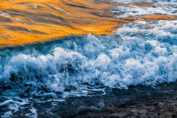 Köpüklü güzel dalgalar, denizin batan güneşiyle aydınlanıyor. Gün batımında dalgalı deniz yüzeyinin dokusu.