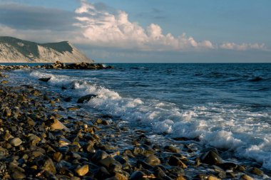 Bulutlu bir akşamda güzel bir deniz manzarası. Dalgalar kayaların üzerinde yuvarlanıyor
