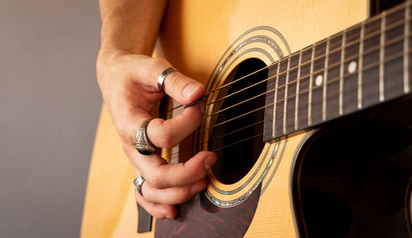 A hand with vintage rings playing and acoustic guitar. Close-up view. Selective focus. Grain.