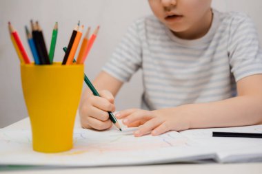 Küçük bir çocuk masaya oturur ve renkli kalemlerle resim çizer.