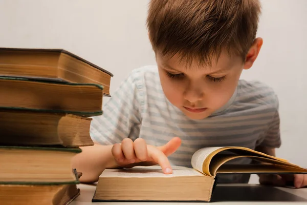 Küçük bir çocuk masada oturur ve bir kitap okur.