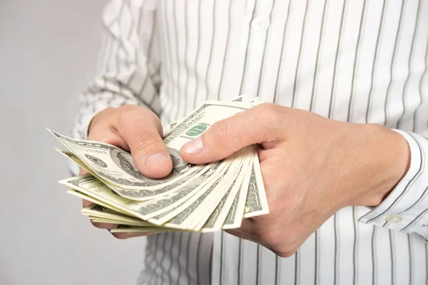 Açık gömlekli bir adam (iş adamı) elinde para tutar. Nakit sayar (100 dolarlık banknotlar).