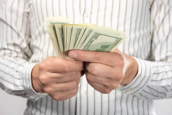 Açık gömlekli bir adam (iş adamı) elinde para tutar. Nakit sayar (100 dolarlık banknotlar).