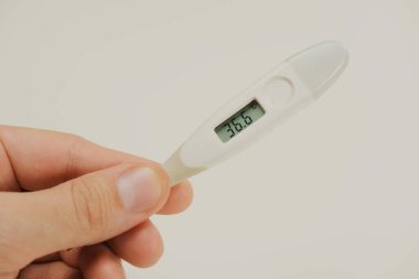 Bir adamın elindeki termometre normal sıcaklığın 36.6 olduğunu gösteriyor.