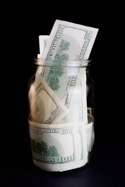 Siyah arka planda cam bir kavanozda dolar banknotları. Kavanozda para tasarrufu