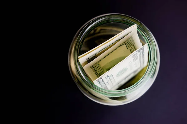 Siyah arka planda cam bir kavanozda dolar banknotları. Kavanozda para tasarrufu
