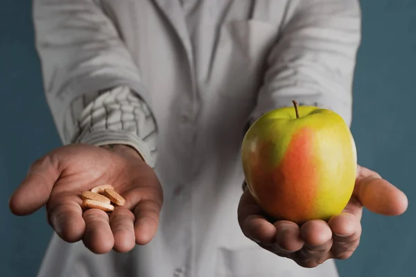 Doktor elinde bir hap ve bir elma tutuyor. Yapay ilaçlar ya da vitaminler ve doğal ürünler arasında seçim yapma kavramı
