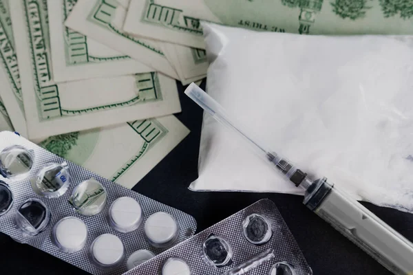 Syringe, powdered substance, pills and money on a black background. The concept of drug addiction, heroin or other drug use