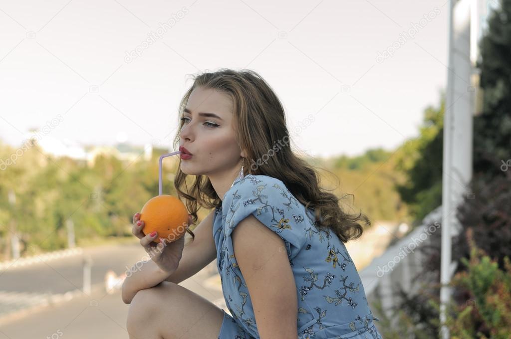 Beautiful girl is drinking juice through a straw from an orange