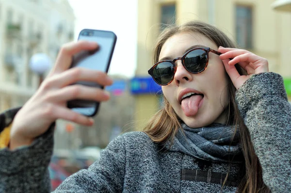 Meisje doet selfie op haar telefoon en tonen van de tong — Stockfoto