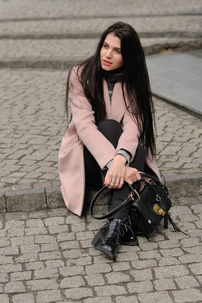 Model shows autumn clothes sitting on the sidewalk