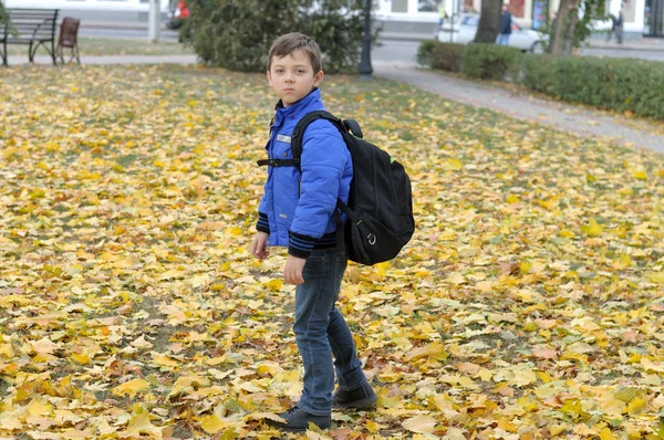 Junge geht mit großem Ranzen über den Rasen zur Schule Stockfoto