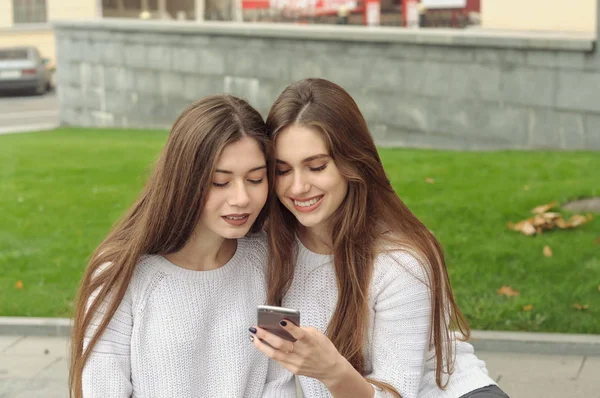 Two brunettes look at photos on their smartphone and laugh — Stok fotoğraf