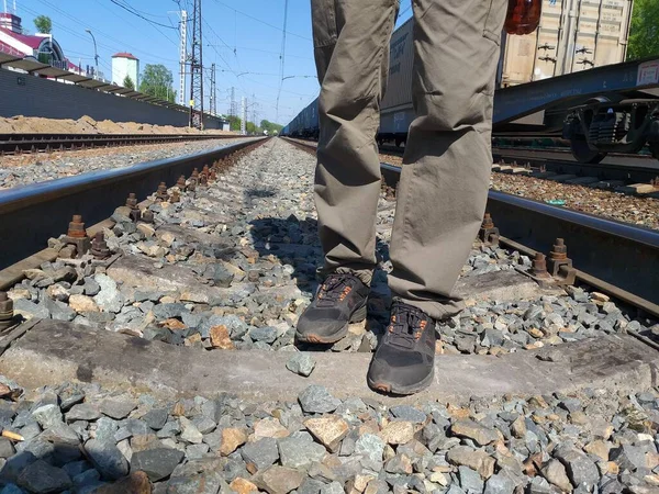 The legs of a lonely man in black sneakers are on the railway. Young male legs walking between empty railway tracks against the background of a moving train. Travel concept. The concept of hope.