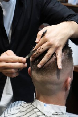  Berber saç makasıyla çalışır. Hipster müşteri saçını kestiriyor. Saç makaslı berber elleri, yaklaşın. Berber dükkanındaki sakallı adam. Saç kesimi konsepti. Berber dükkanında kuaförü ziyaret eden bir adam..