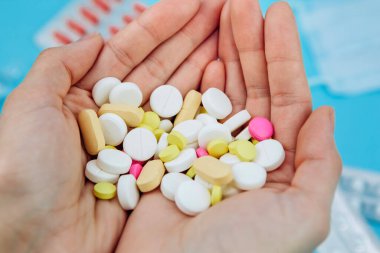 Doktorun elinde haplar var. Coronavirus için tedavi. Covid-19 'a karşı verilen savaşta tıbbi ilaçlar. Haplar, şırıngalar, termometre, mavi masada tıbbi maske. kavramsal tıbbi geçmiş.