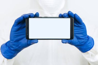 Koruyucu giysili doktor, solunum cihazı, gözlük, eldiven bir tablet / telefon tutuyor. Mesaj için yer. Doktorlar koronavirüs salgını sırasında evde kalmalarını tavsiye ettiler. COVID-19