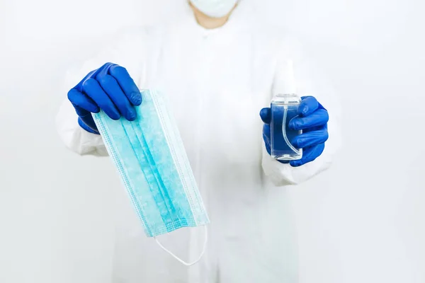 Elinde dezenfektanla beyaz arka planda duran tıbbi maskeli bir doktor. Coronavirüs salgınında dezenfektan kullanımı. COVID 2019. Doktorlara yardım et - evde kal.