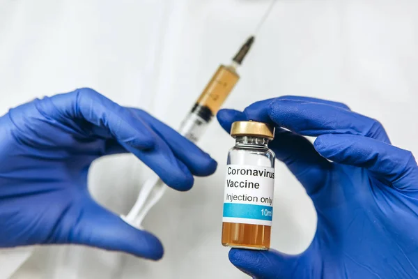 Beyaz cüppeli ve mavi eldivenli bir doktor, içinde koronavirüs aşısı olan bir şırınga tutuyor. Covid-2019 'dan aşı enjekte edildi. Pandemik koronavirüs 2020. Aşı testi.