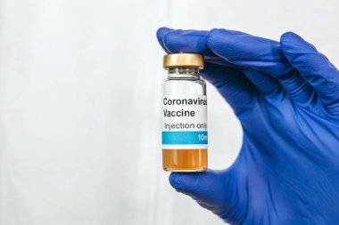 Doktor beyaz arka planda Coronavirus aşısı olan bir test tüpü tutuyor. Covid-19 aşısı. 2020 Salgını. Doktorun elleri mavi tıbbi eldivenlerde. Virüsün tedavisi..